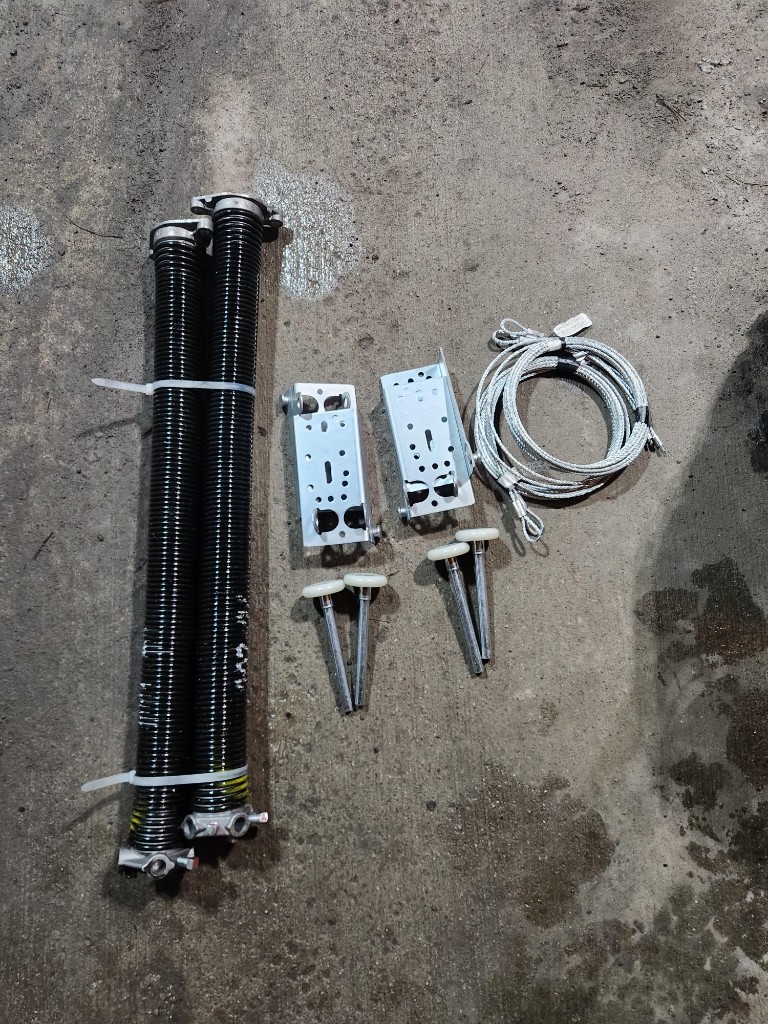 Complete garage door rebuild parts — new torsion springs, bottom brackets, lift cables, and roller pins for a Stittsville job