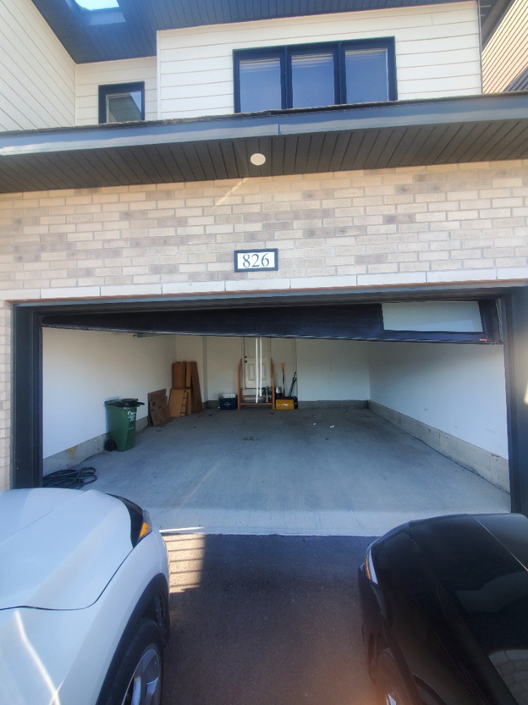 Garage door jammed open on a Stittsville townhome after coming off track, looking into the garage from the driveway