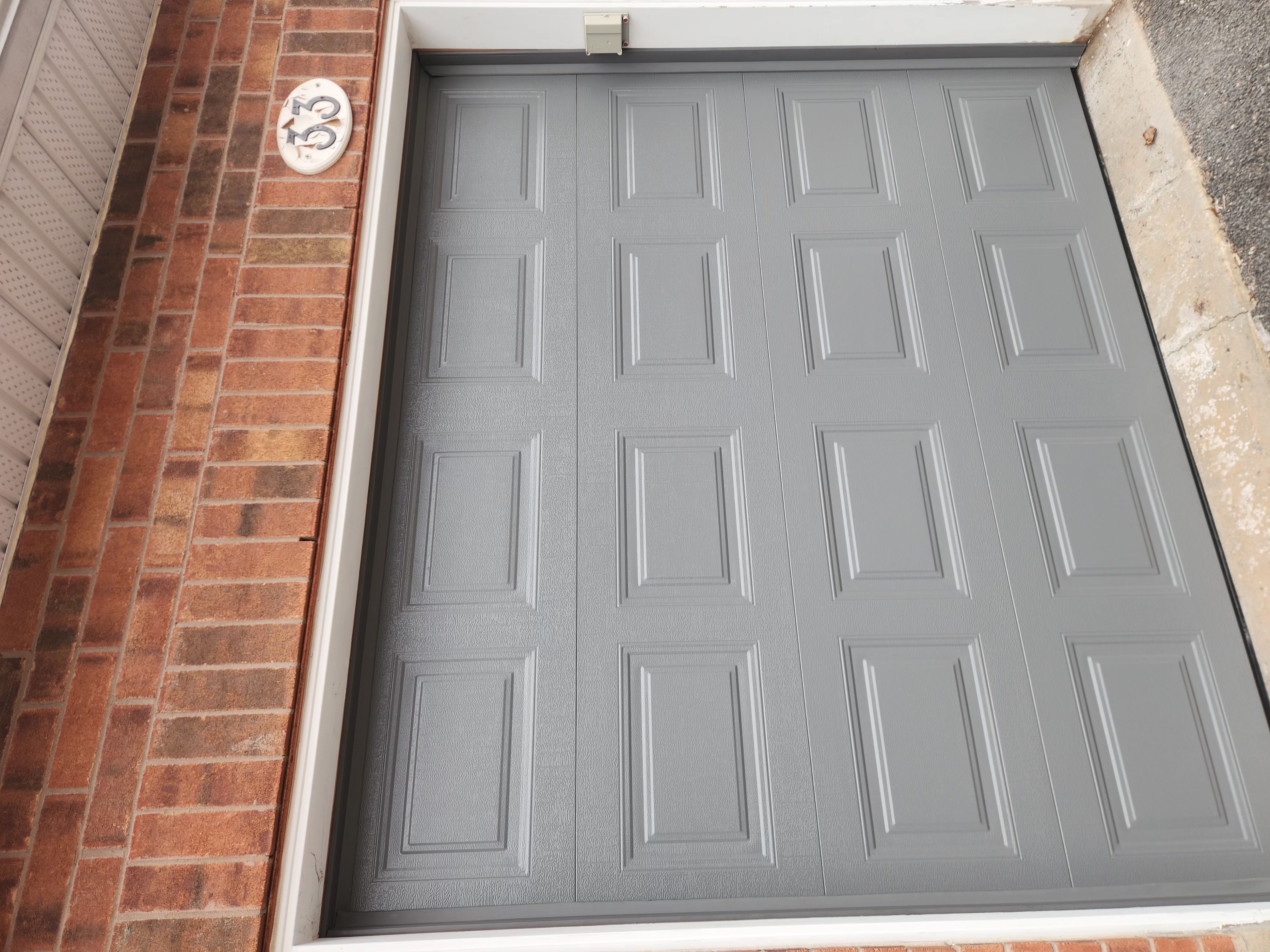 New grey short-panel single-car garage door installed on brick townhome
