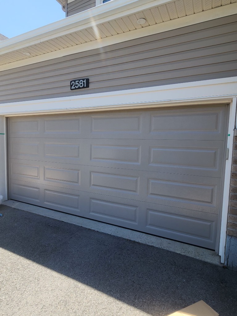New light grey raised-panel double garage door installed on a Stittsville-area home with lap siding and white trim