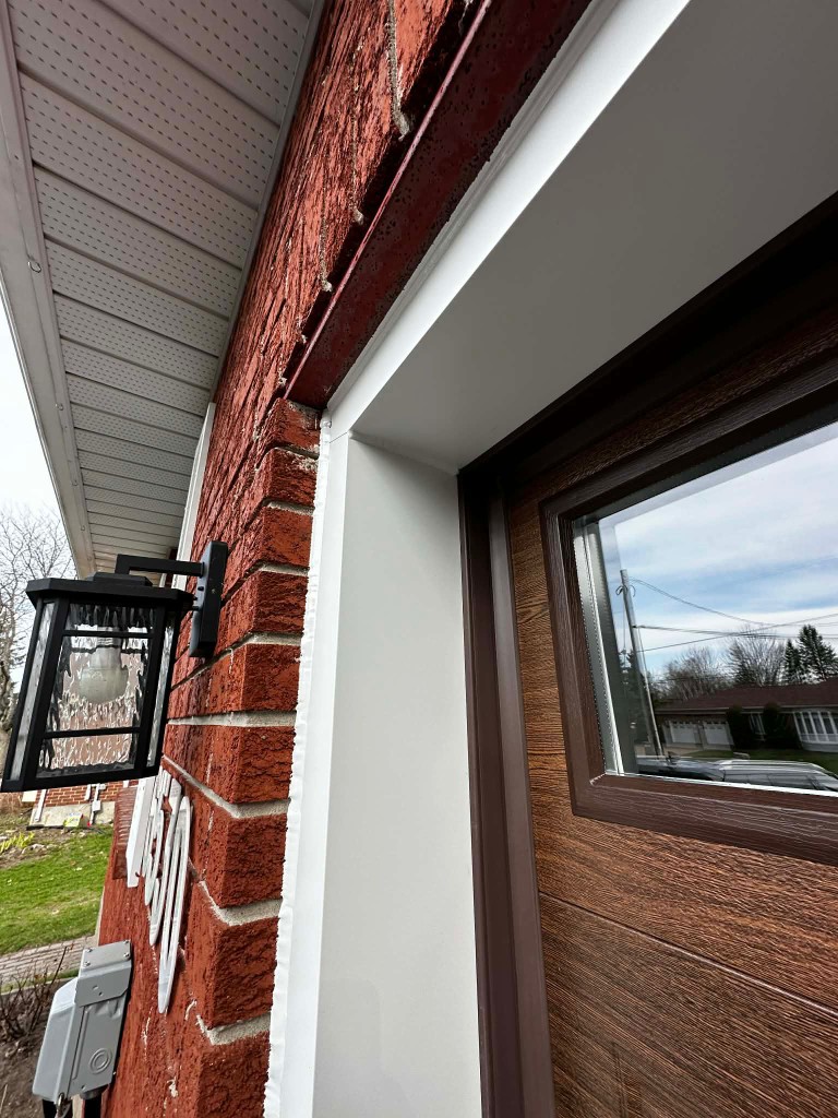 Close-up of new white perimeter weather stripping installed along the brick frame of a wood-look garage door on a Stittsville home