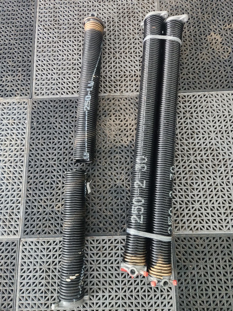 Several sets of torsion springs laid out on garage floor tiles, ready for Stittsville same-day spring replacements