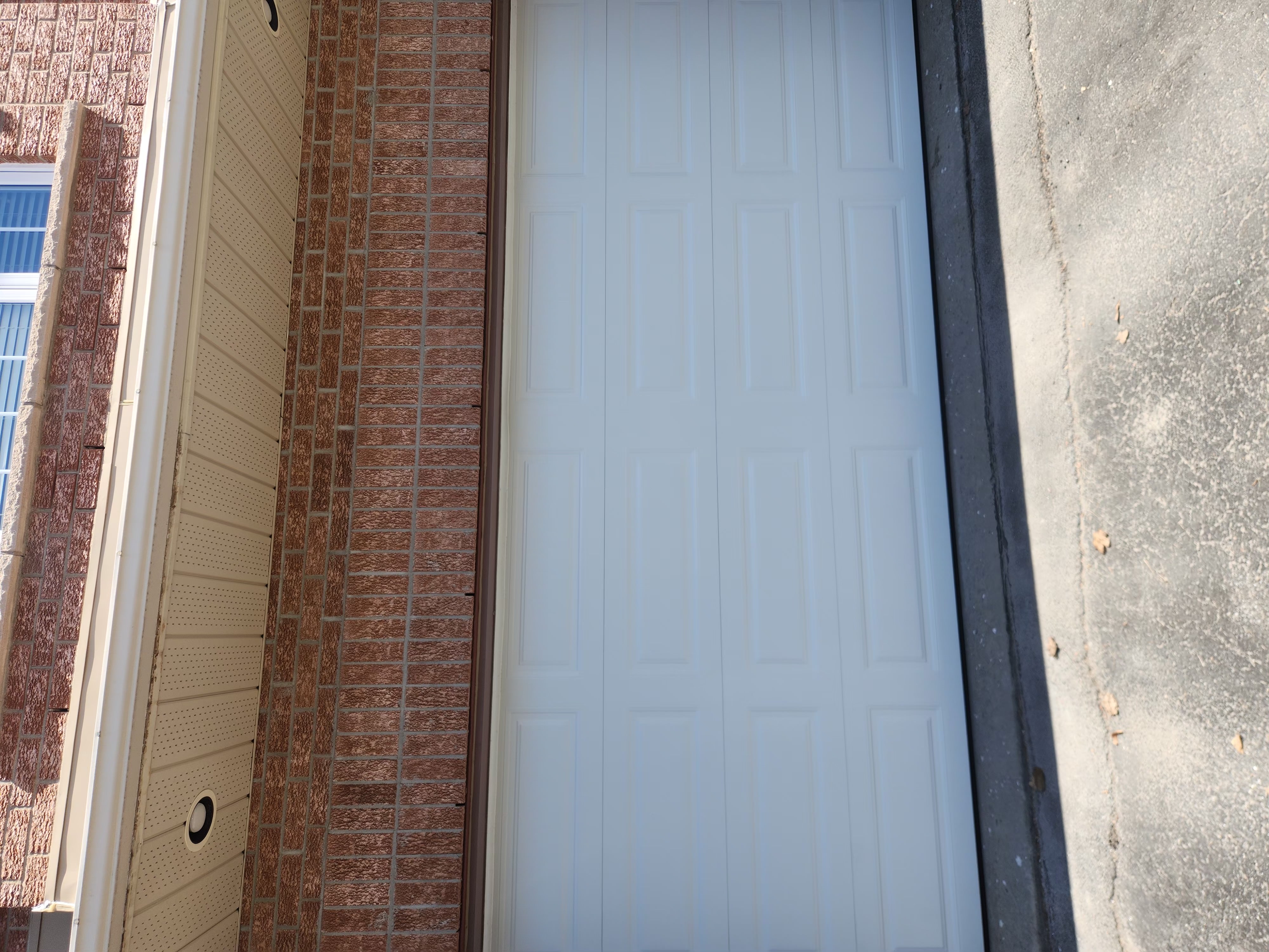 New white long-panel double-car garage door installed on brick home