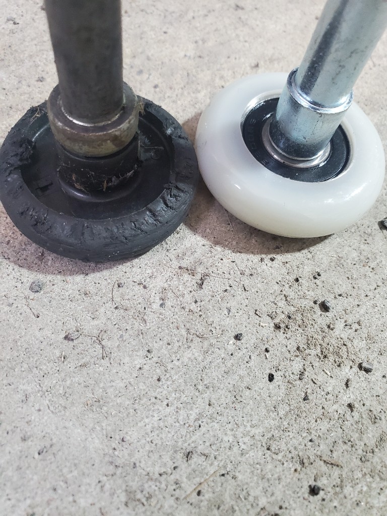 Side-by-side comparison of a worn black rubber garage door roller next to a fresh nylon roller on a Stittsville driveway